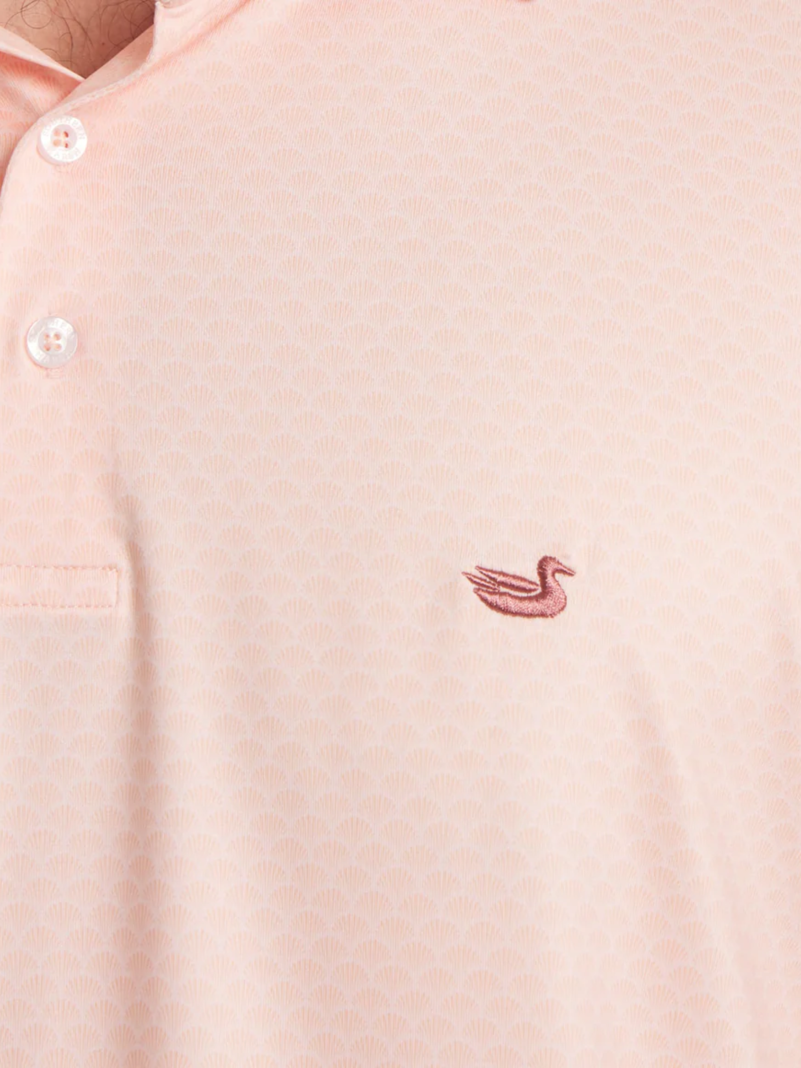 Close-up of a coral polo shirt with a small logo on the chest and shell pattern 