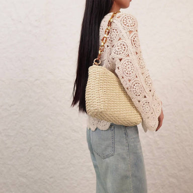 Person wearing a white lace top and light blue jeans, holding a beige woven handbag 